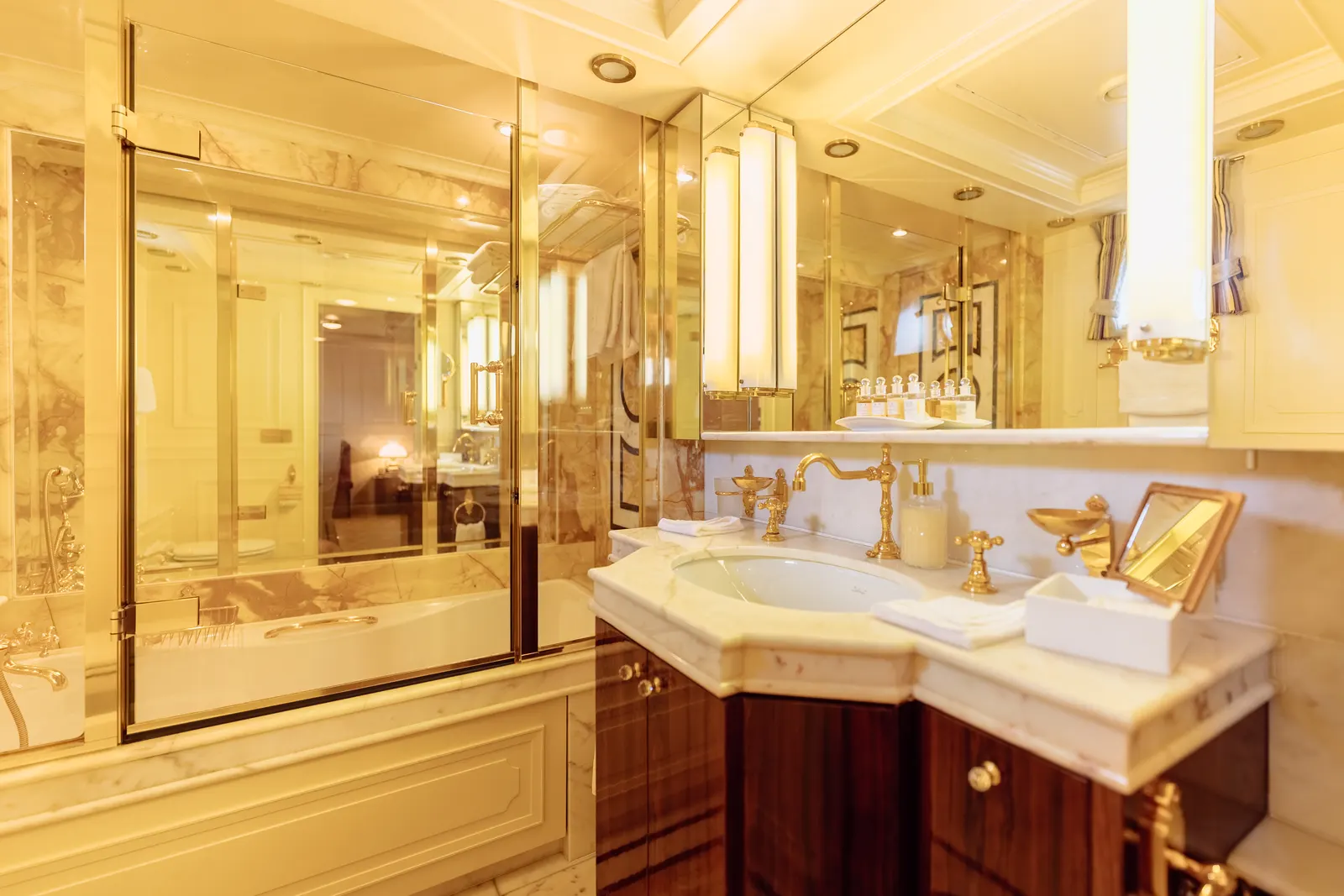 A bathroom basin and bath in marble with gold taps and framed mirrors.