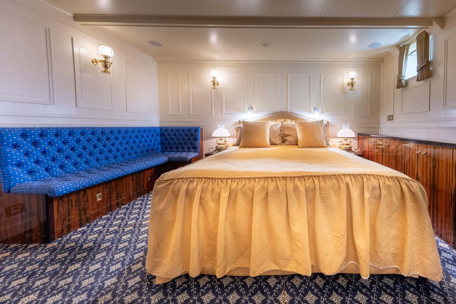 A cabin with a buttoned blue bench seat and a gold bed cover.