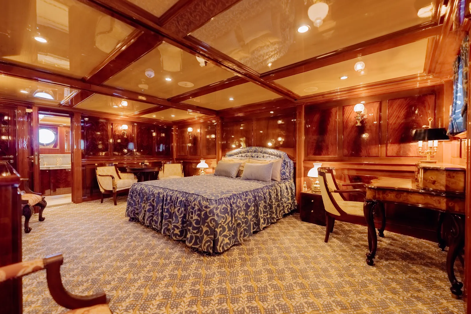A suite with a blue patterned bedspread, mahogany panelling and a writing desk.