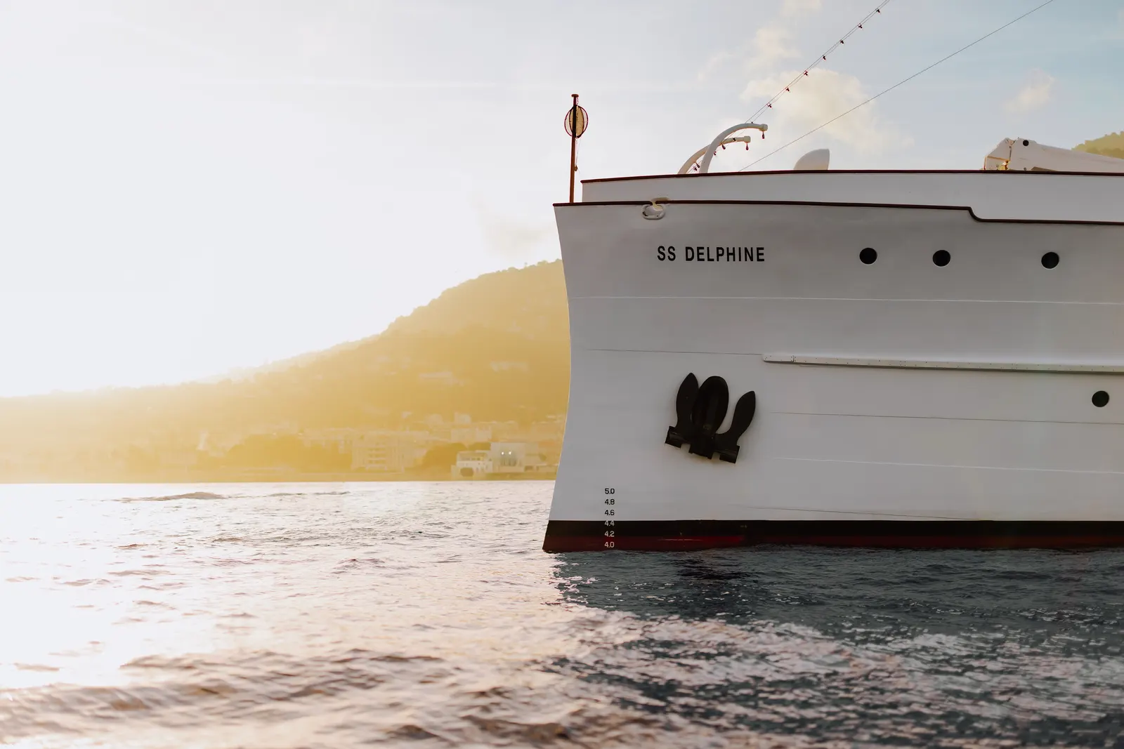 The bow of SS Delphine with her name on the hull, a hazy coastline beyond.