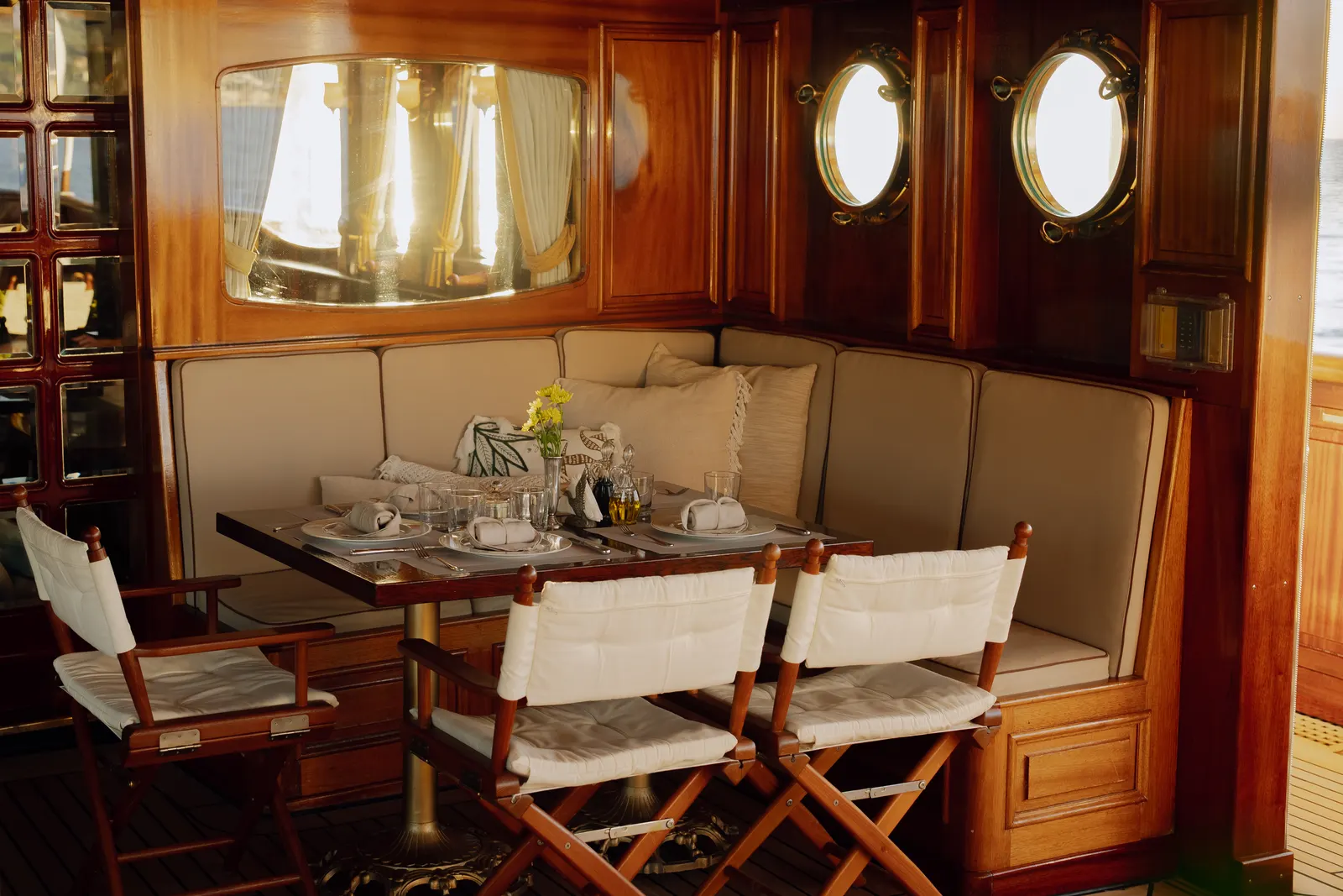 A banquette table set for breakfast beside two portholes.