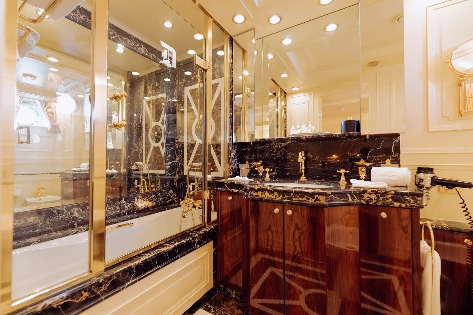 A bathroom lined in dark marble, with a bath beneath mirrored panels.
