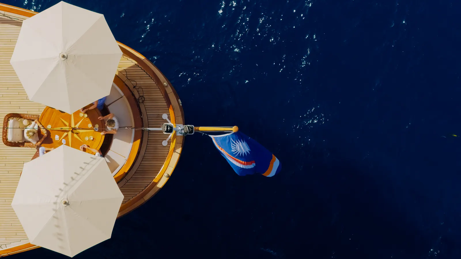 Looking straight down on the aft deck of SS Delphine, its parasols open and the ensign streaming over blue water.