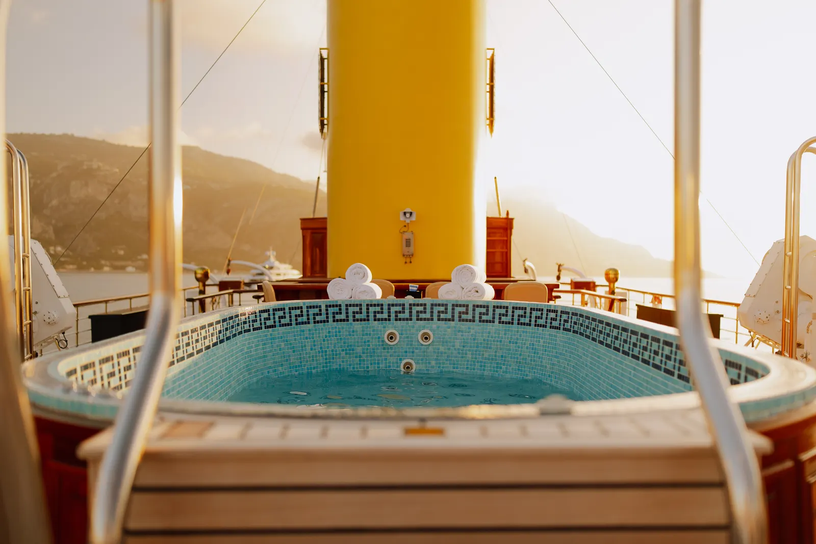 The tiled deck pool of SS Delphine below her yellow funnel, hills across the water.