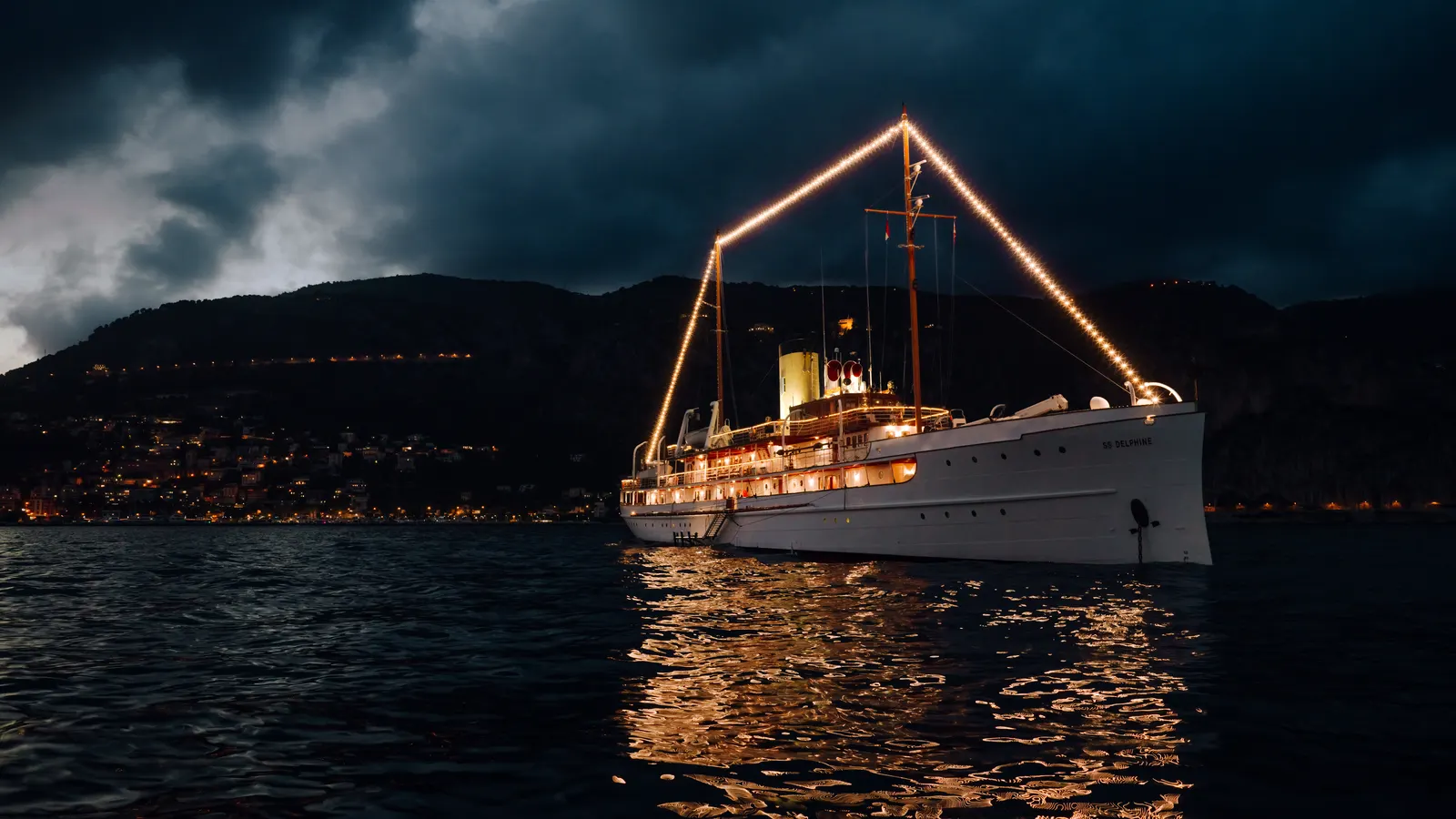 SS Delphine lit from stem to stern after dark, her reflection long on the water.