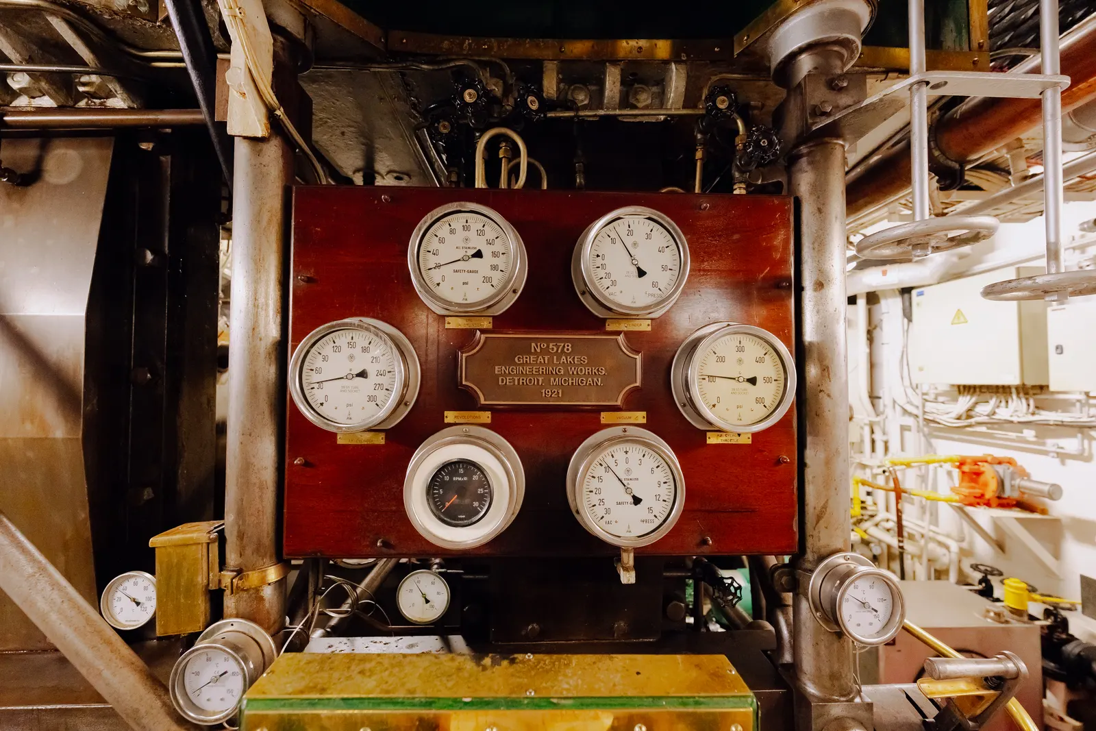 Engine room gauges and valves mounted on a varnished board.