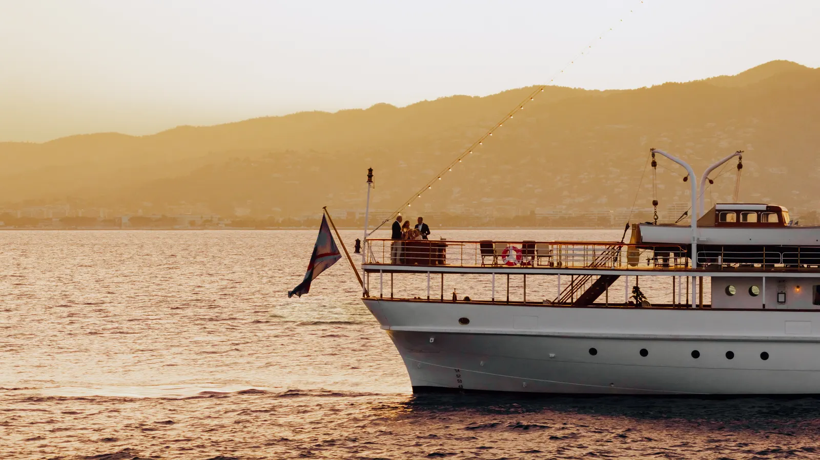 Guests at the rail of SS Delphine as the sun drops behind the hills.