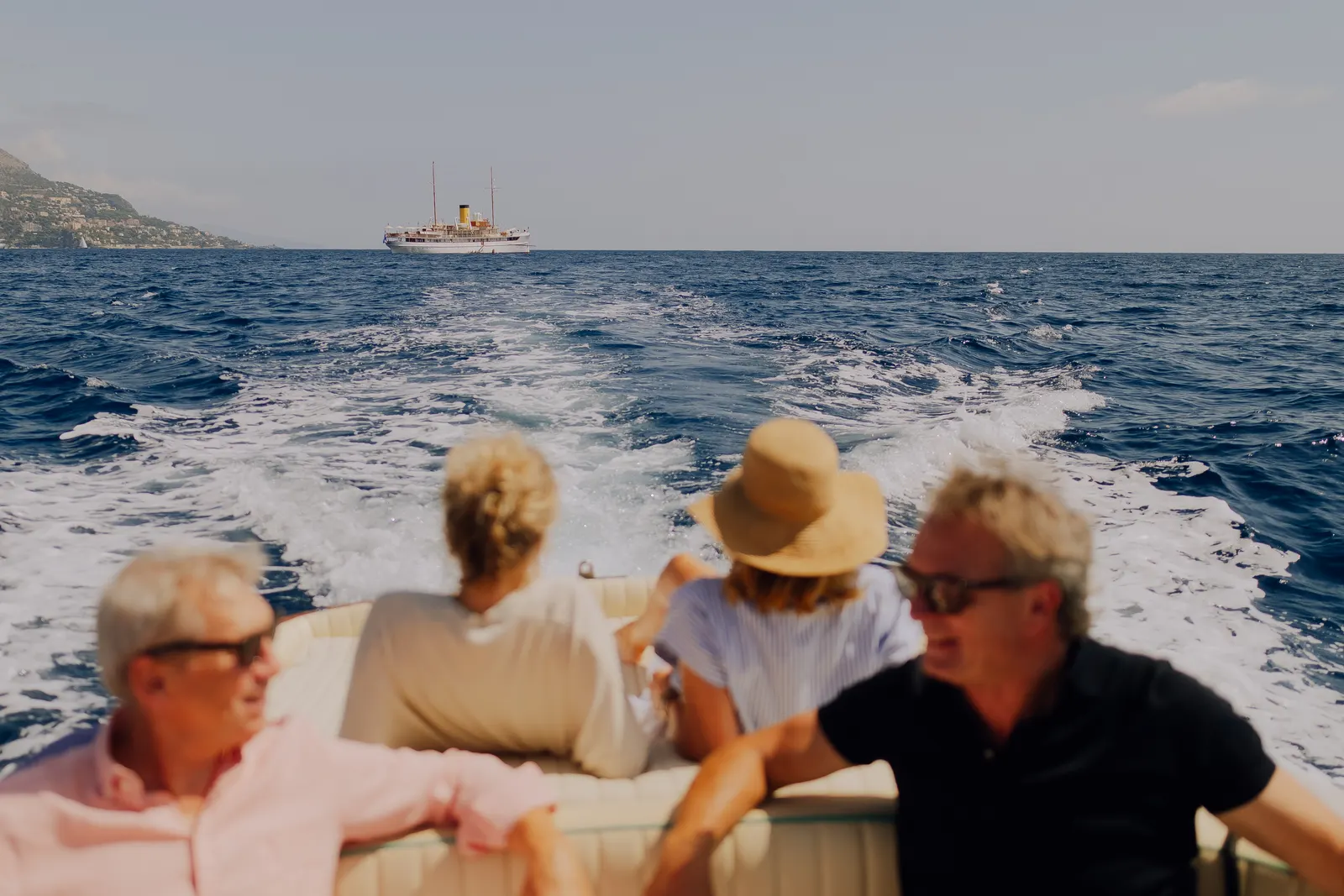 Four guests at the stern rail watching the wake, with SS Delphine on the horizon.