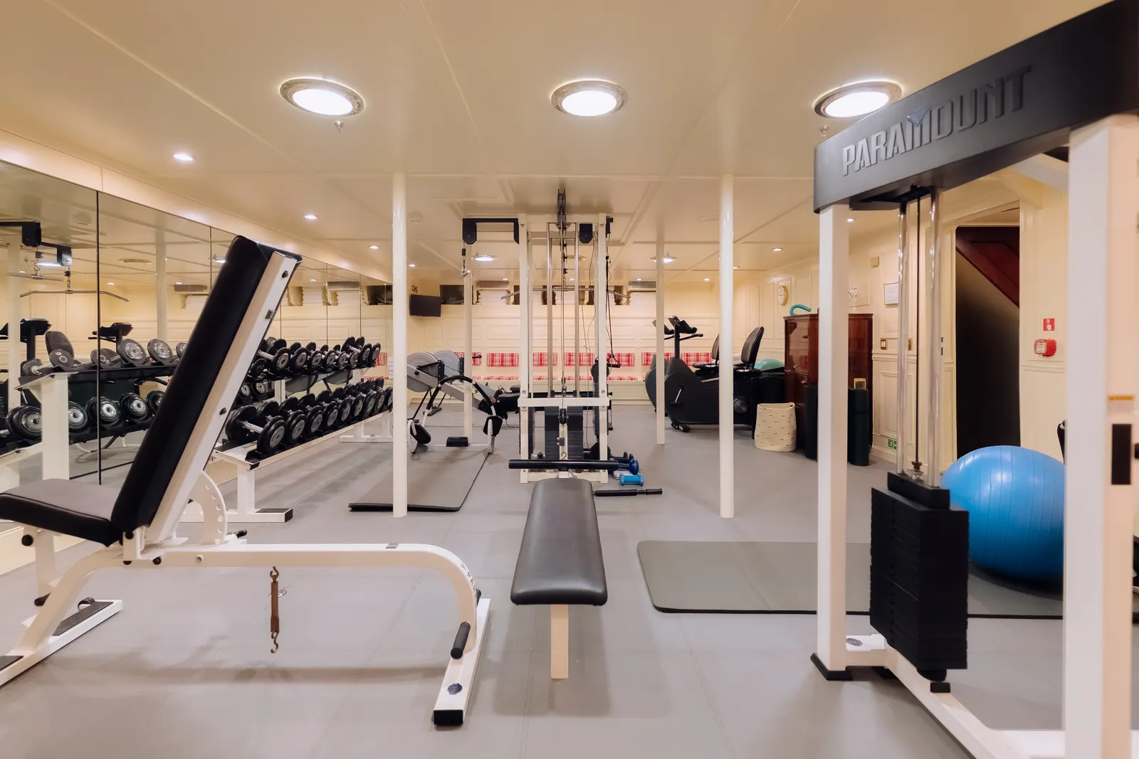 The gym, with free weights, benches and a mirrored wall.