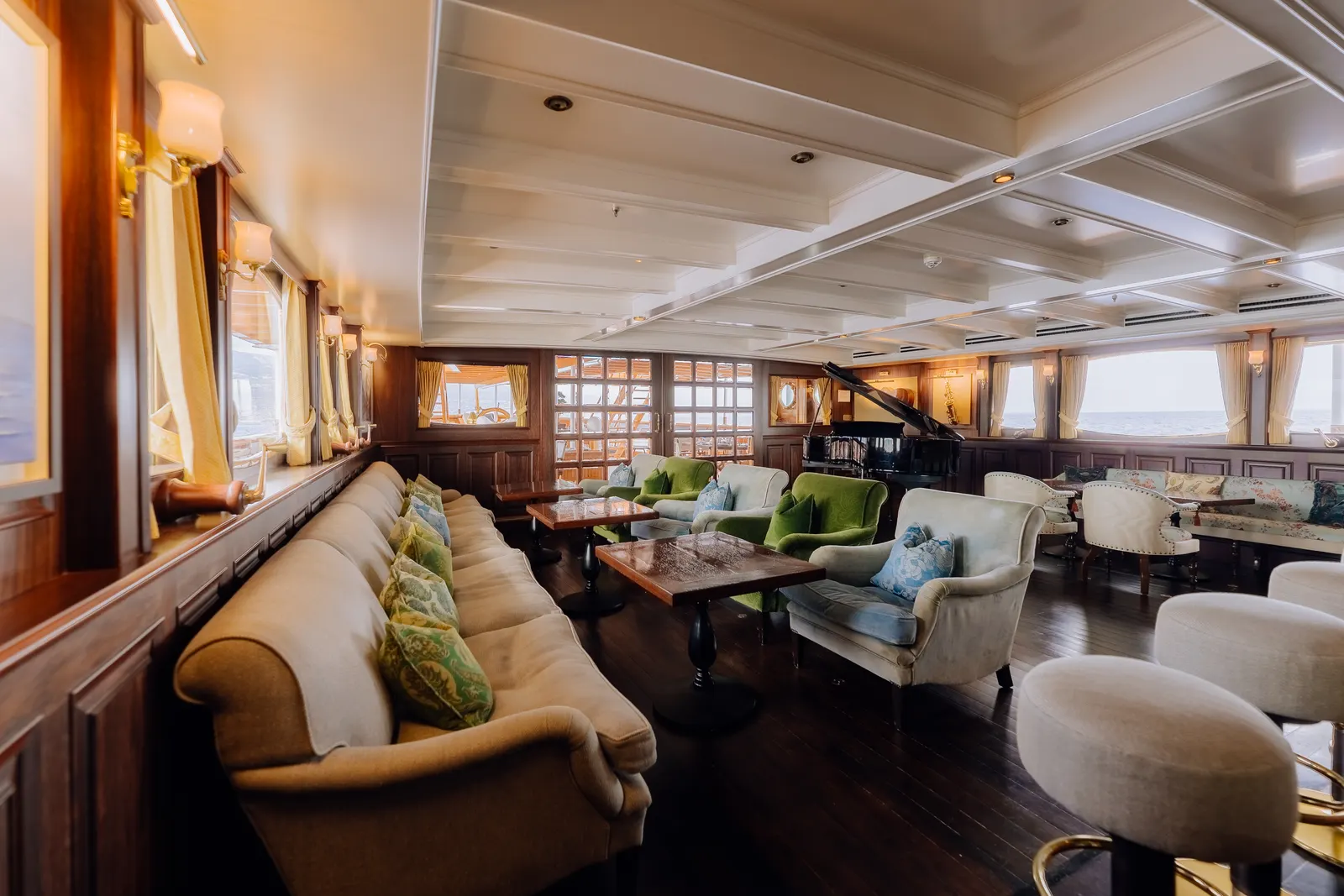 The main salon of SS Delphine, cream sofas and armchairs running the length of the windows under a coffered ceiling.