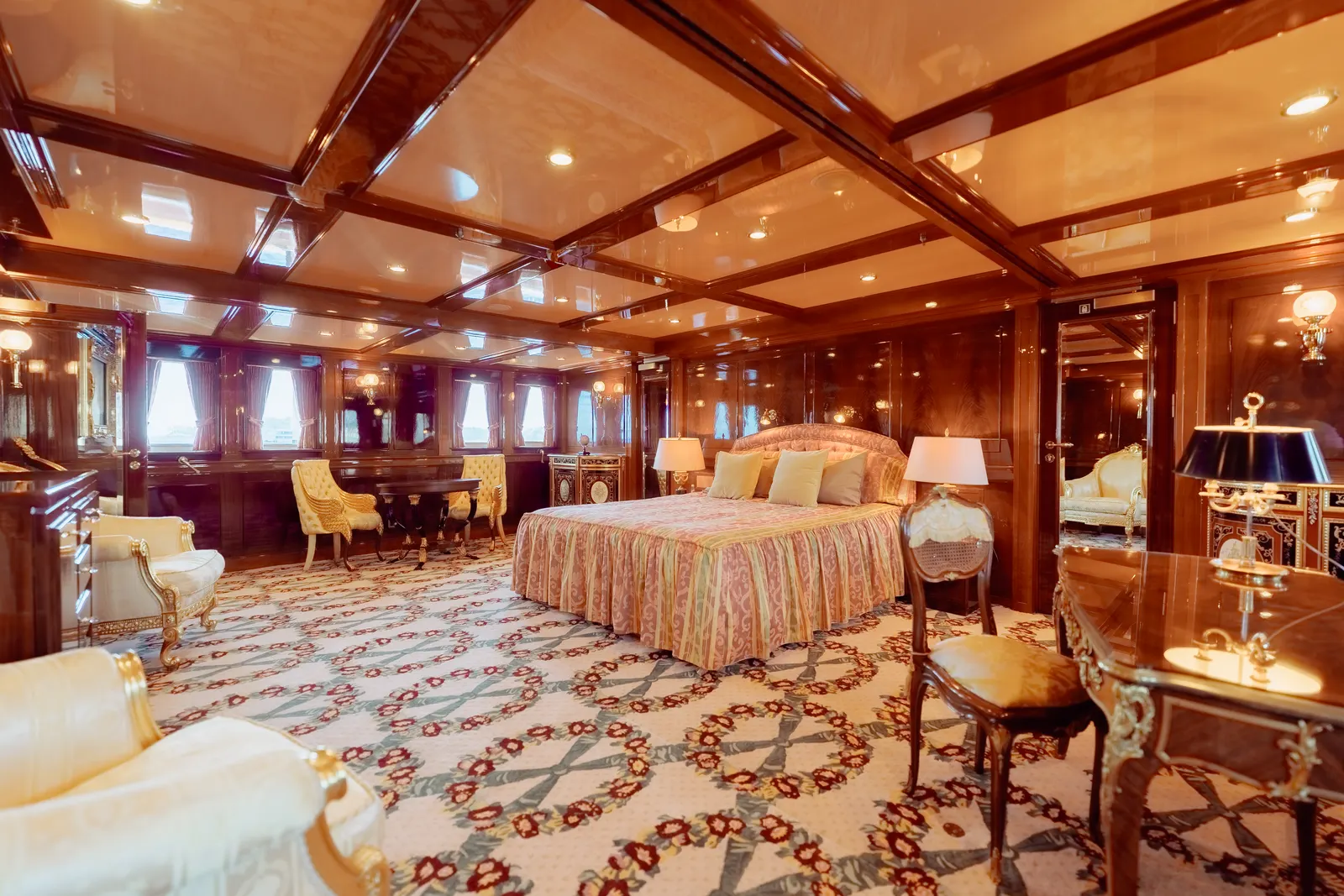 A panelled suite with a king bed, armchairs and a writing desk under a mahogany coffered ceiling.