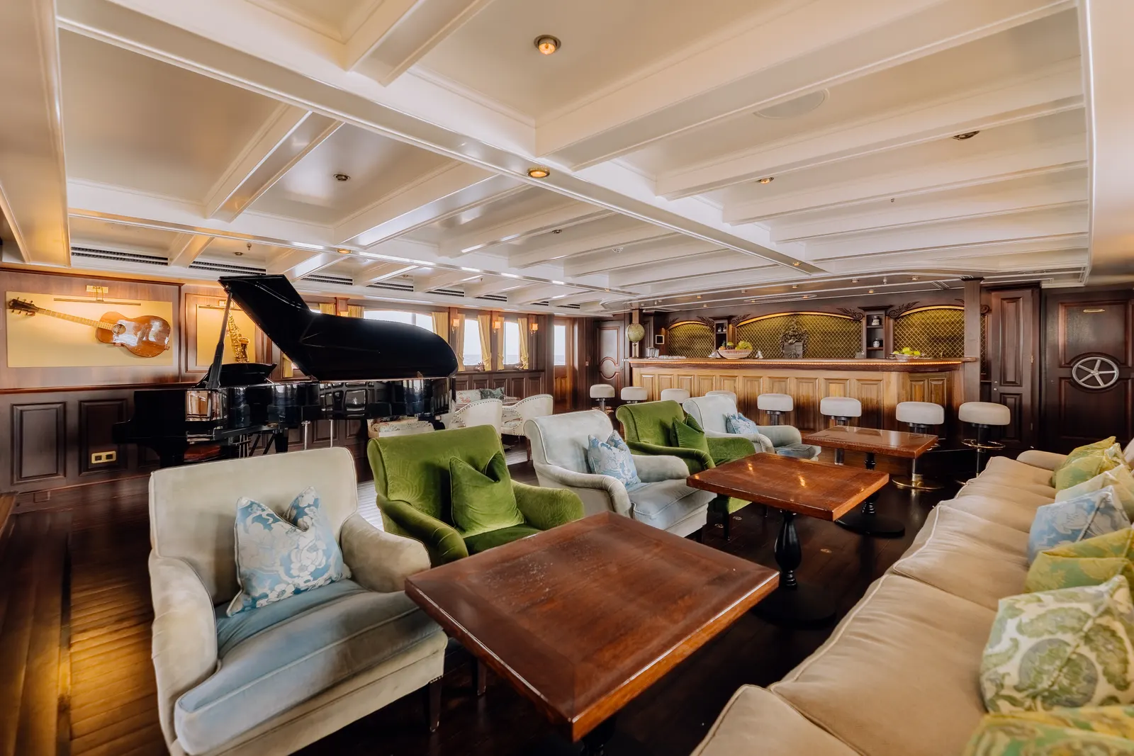 The Music Room aboard SS Delphine, its grand piano at the far end beyond green and cream seating.