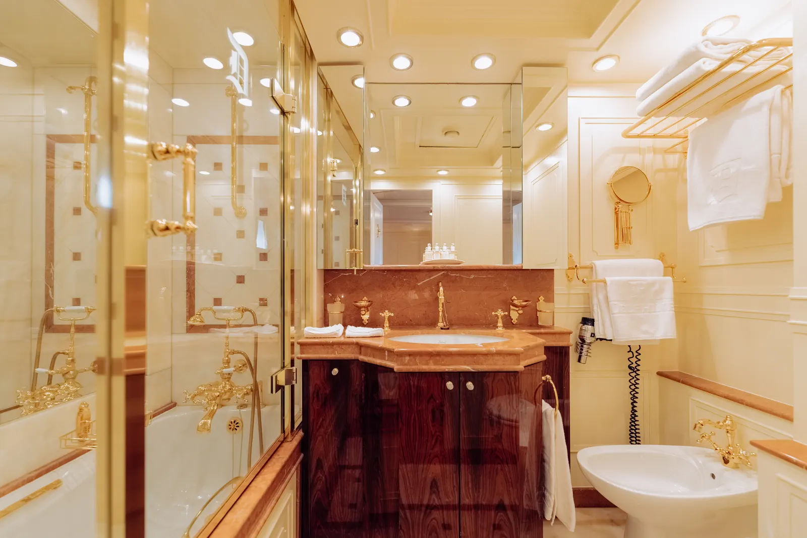 A bathroom with a glazed shower, mahogany vanity and folded towels.