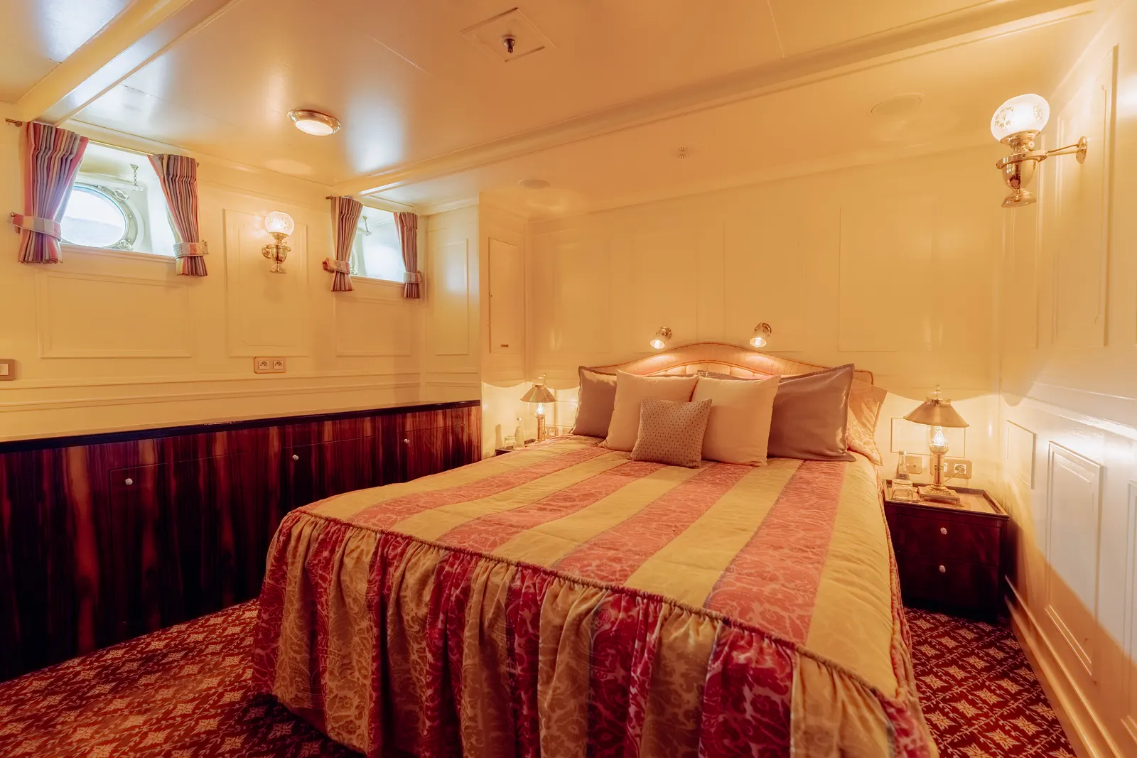 A cabin dressed in red and gold striped textiles, with curtained portholes.