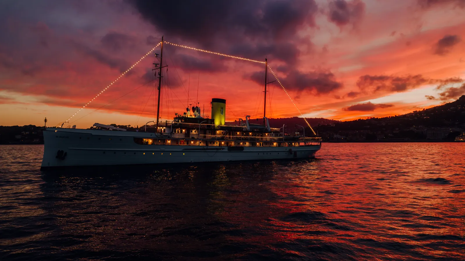 SS Delphine silhouetted at anchor under a red sunset sky.