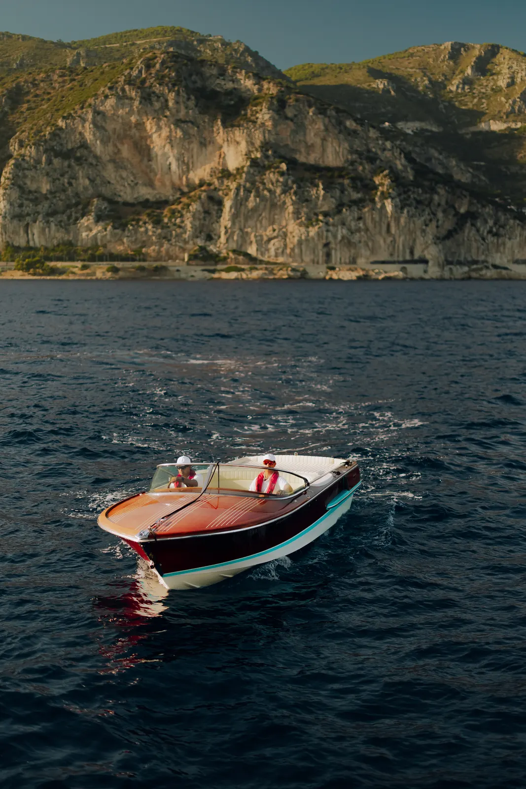 A varnished classic tender running across open water with her driver at the wheel.