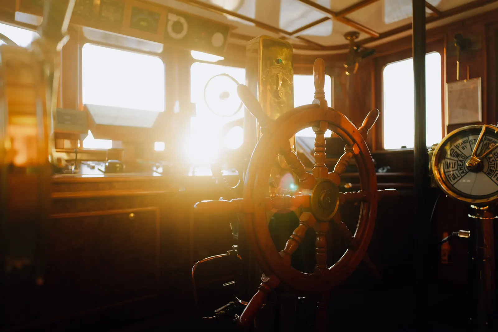 The ship's wheel and telegraph in the wheelhouse with the sun low in the windows.